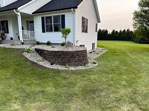 Finished stacked-stone planter bed with river rock and a new tree after service